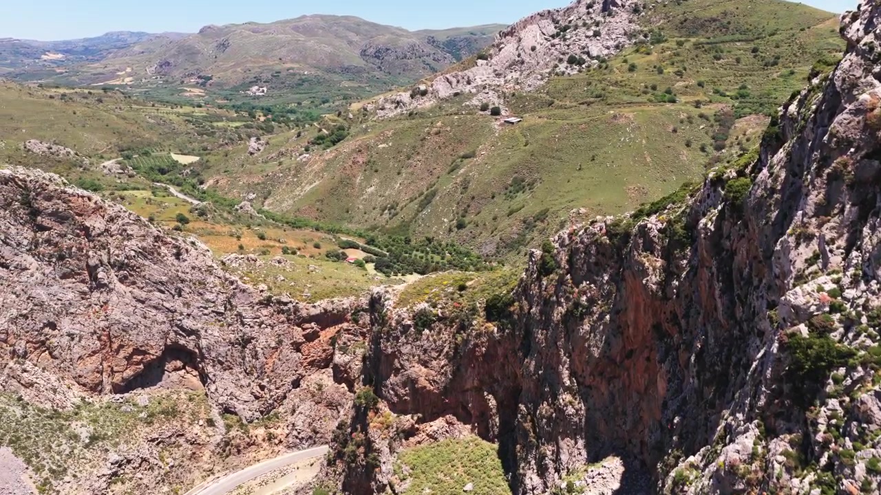 Vista aérea con dron de un desfiladero rocoso que se abre a un valle verde con montañas al fondo, Garganta de Kourtaliotiko, Grecia
