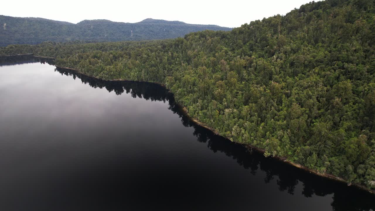 Tranquil Waters Of Lake Mapourika Surrounded By Dense Green Forested Hill On West Coast Of New Zealand's South Island. aerial shot