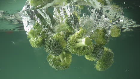 slow motion of fresh raw broccoli falling into water on green background