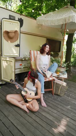 two women relaxing and playing ukulele at a camper van