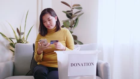 woman pressing phone using a credit card to pay online to reserve donation box delivery