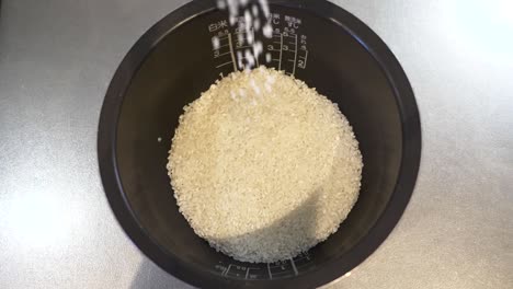 above angle slow motion shot of short grain rice poured into a rice cooker bowl in a kitchen