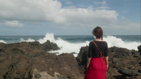 woman admires the huge waves crashing on the rocky shore