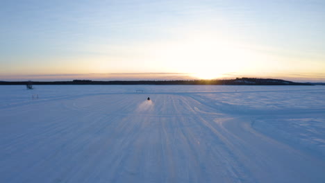 vista aérea conductor solitario de motos de nieve que viaja rápido a través del desierto de invierno nórdico nevado hacia el amanecer