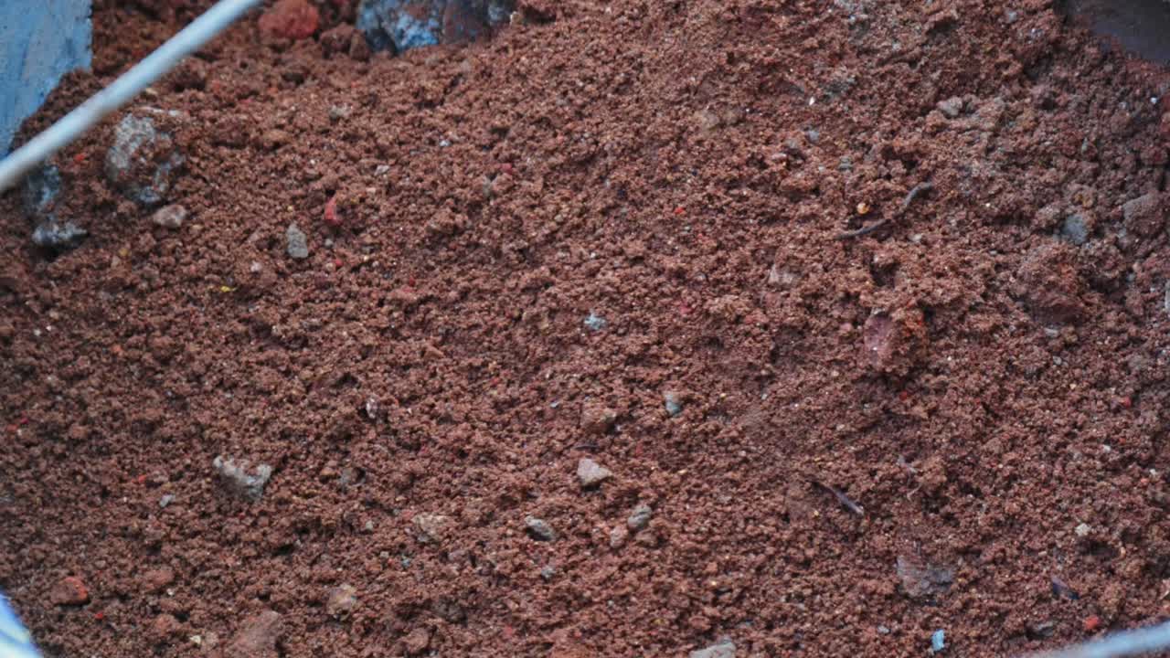 Operaio che usa terra rossa per riempire un buco nell'area delle fondazioni in cantiere. Di giorno, ripresa ravvicinata e stabile, 4k.