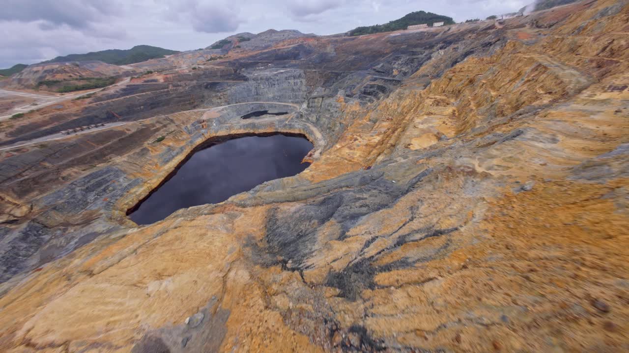 FPV drone flight over open-pit gold and silver mine in Cotui, Dominican Republic. Cloudy day in rocky landscape.