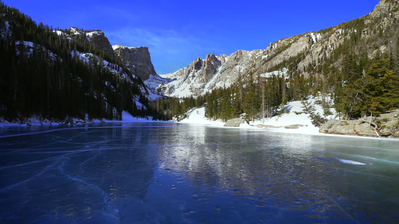 Jäänsininen sävy Dream Lake -järvellä, Coloradon Rocky Mountainin kansallispuiston (RMNP) Emerald Lake -järvellä, aurinkoinen sininen taivas, Hallett Peak, Flattop Mountains, Estes Park, Bear Lake -vaellusreitti, tuiskuttava lumi, tuulinen, lähennys.