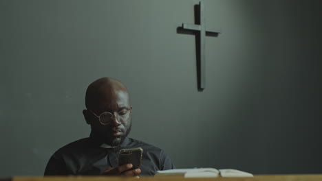 black catholic priest using mobile phone in modern church