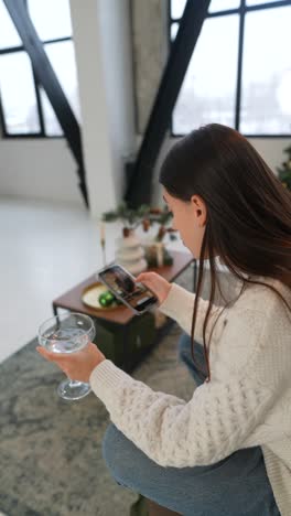 woman relaxing in a modern apartment, using smartphone and drinking a cocktail.