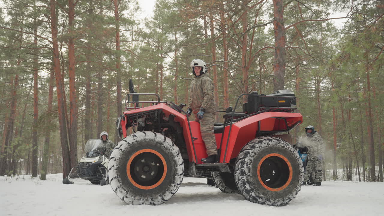 ATV rosso in una foresta innevata, pilota con casco che percorre un sentiero tra i pini, grandi pneumatici tassellati che sollevano neve, luce fredda e nuvolosa, rombo del motore, equipaggiamento invernale, atmosfera da guida fuoristrada, avventura estrema all'aperto.
