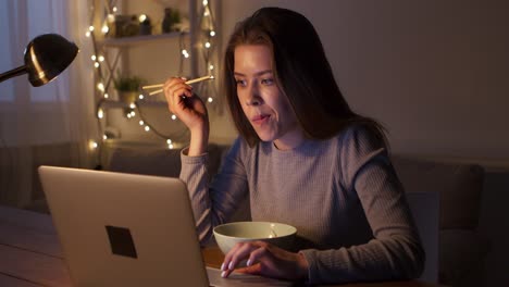 woman eating noodles and working on laptop at night