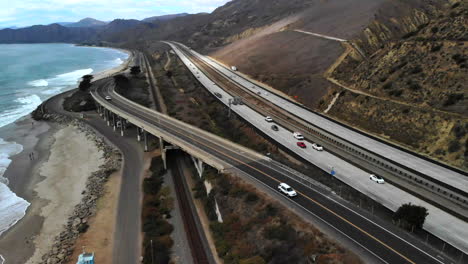 aerial drone shot over the top of a concrete bridge on the beach in ventura next to the ocean waves and the california 101 freeway along the coast