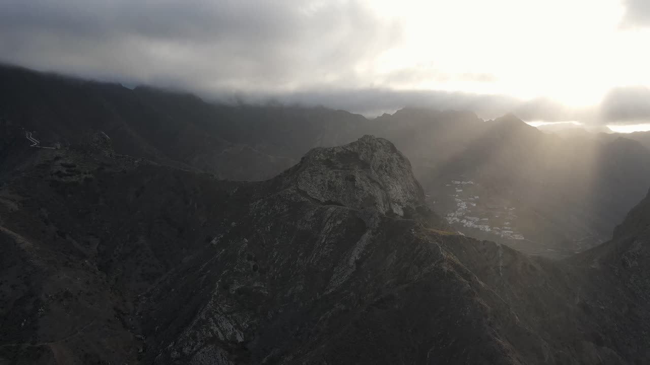 imágenes de los rayos del sol a través de las nubes que iluminan una montaña rocosa en la isla volcánica de tenerife