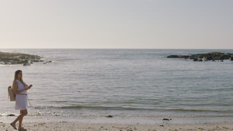 young woman walking on sunny beach taking photo enjoying relaxed vacation