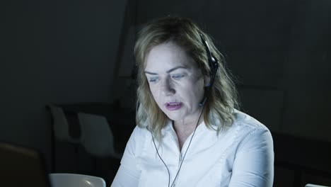 Serious-woman-in-headset-working-in-dark-office