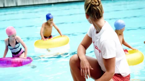 Female-lifeguard-looking-at-students-playing-in-the-pool