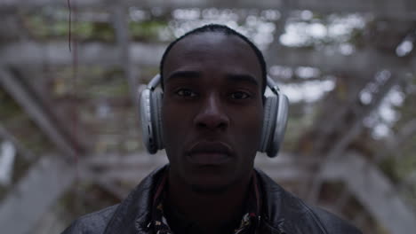 hombre negro de aspecto confiado y fresco en un entorno de jardín urbano usa auriculares inalámbricos