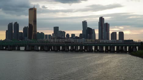 sunset over han river in seoul, south korea with view of 63 building train moving on railway bridge