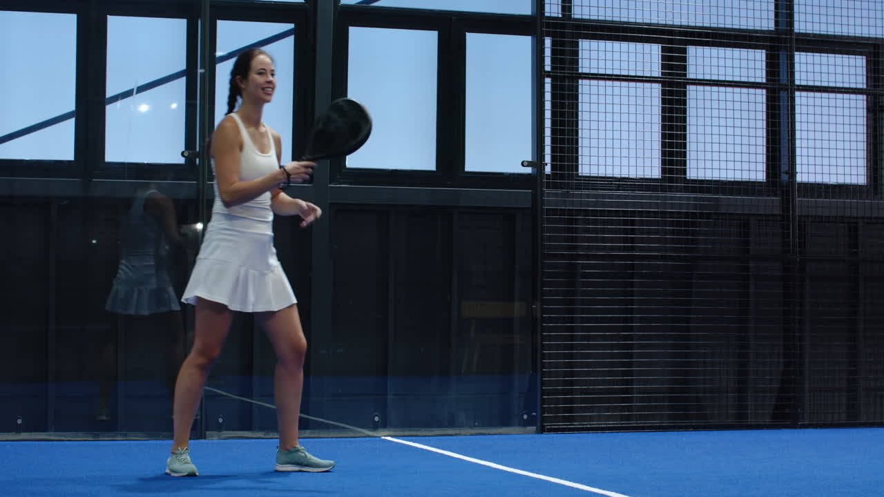 Woman playing padel tennis, smiling and holding racket on blue indoor court