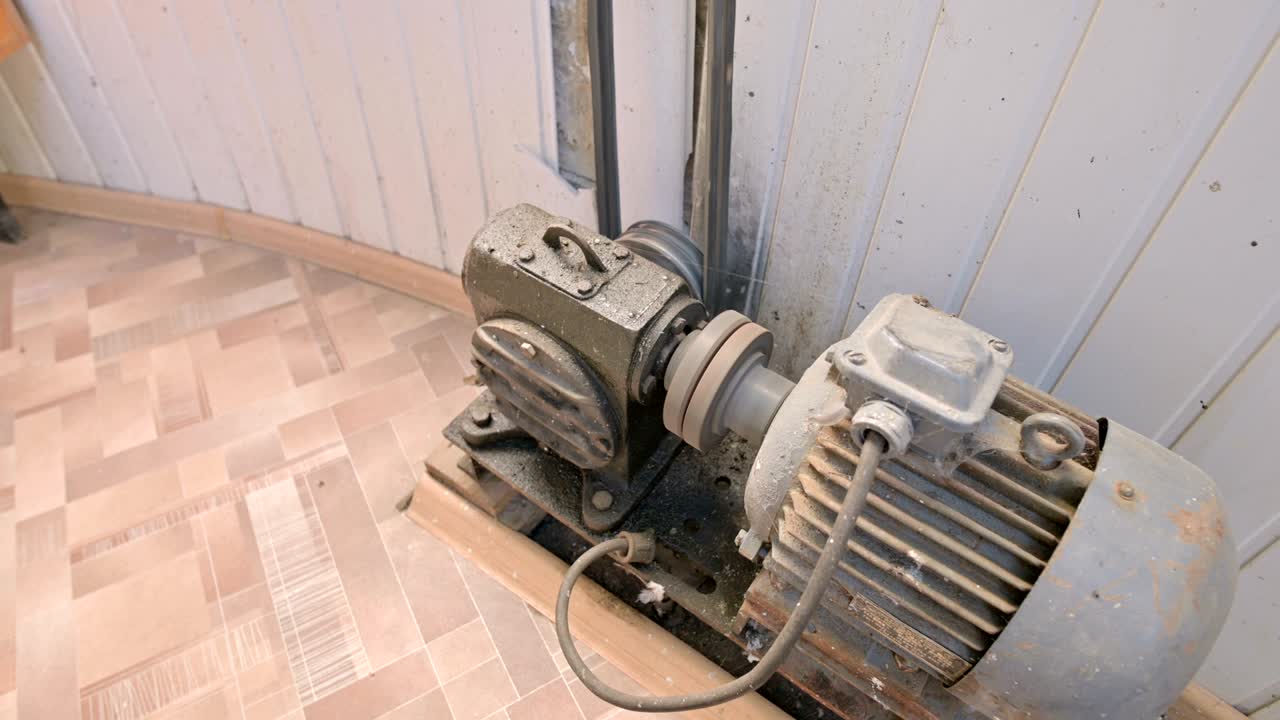 un vecchio motore elettrico coperto di polvere e sporcizia gira una puleggia a due fili attraverso una scatola di ingranaggi cardan con un'azionatura a cinghia a un altro meccanismo. il concetto di vecchi motori elettrici e attrezzature