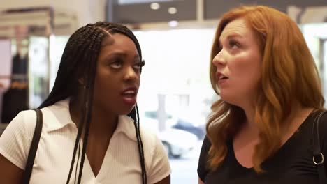 two women engaged in a focused conversation while shopping, examining items together in a retail environment, deeply discussing their choices