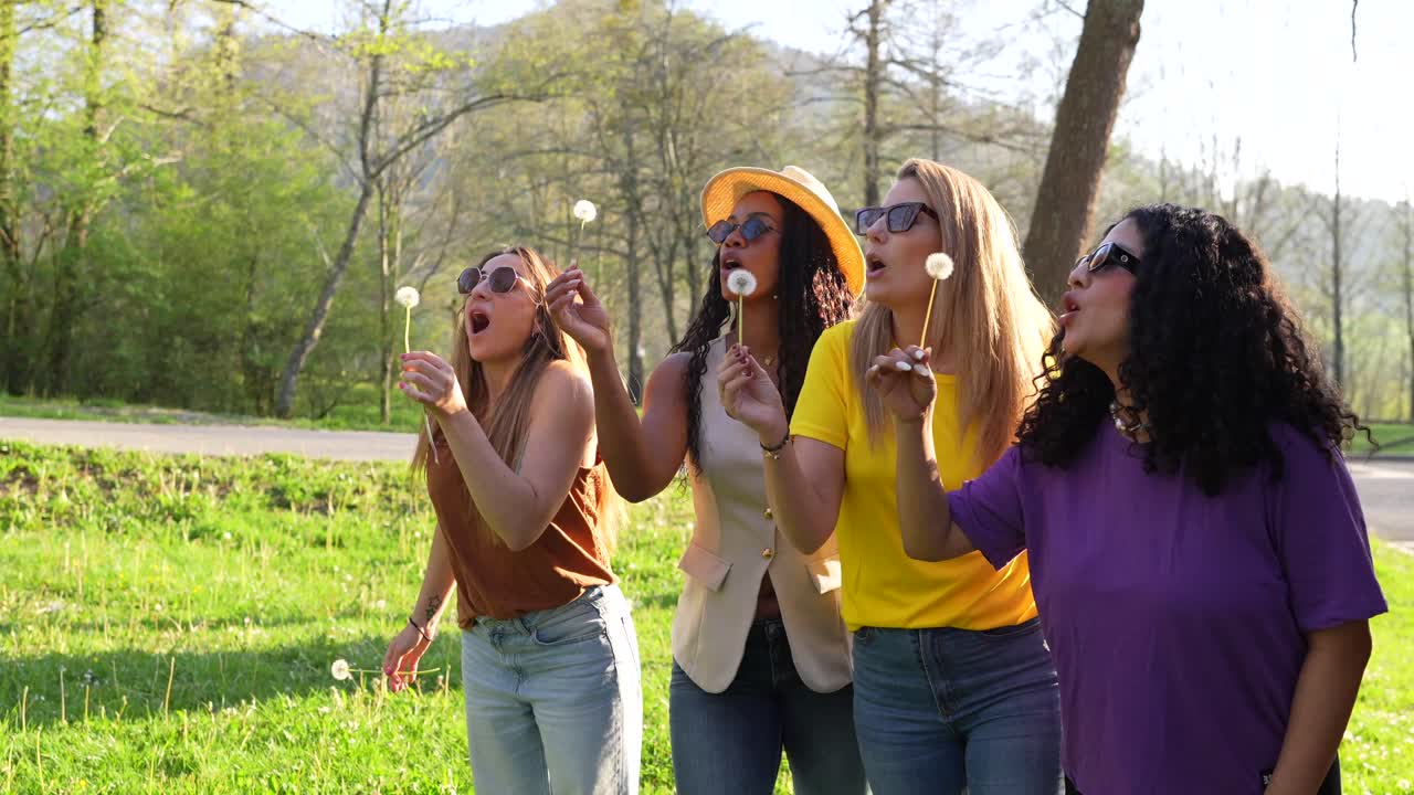 Group of friends blowing dandelions in a meadow