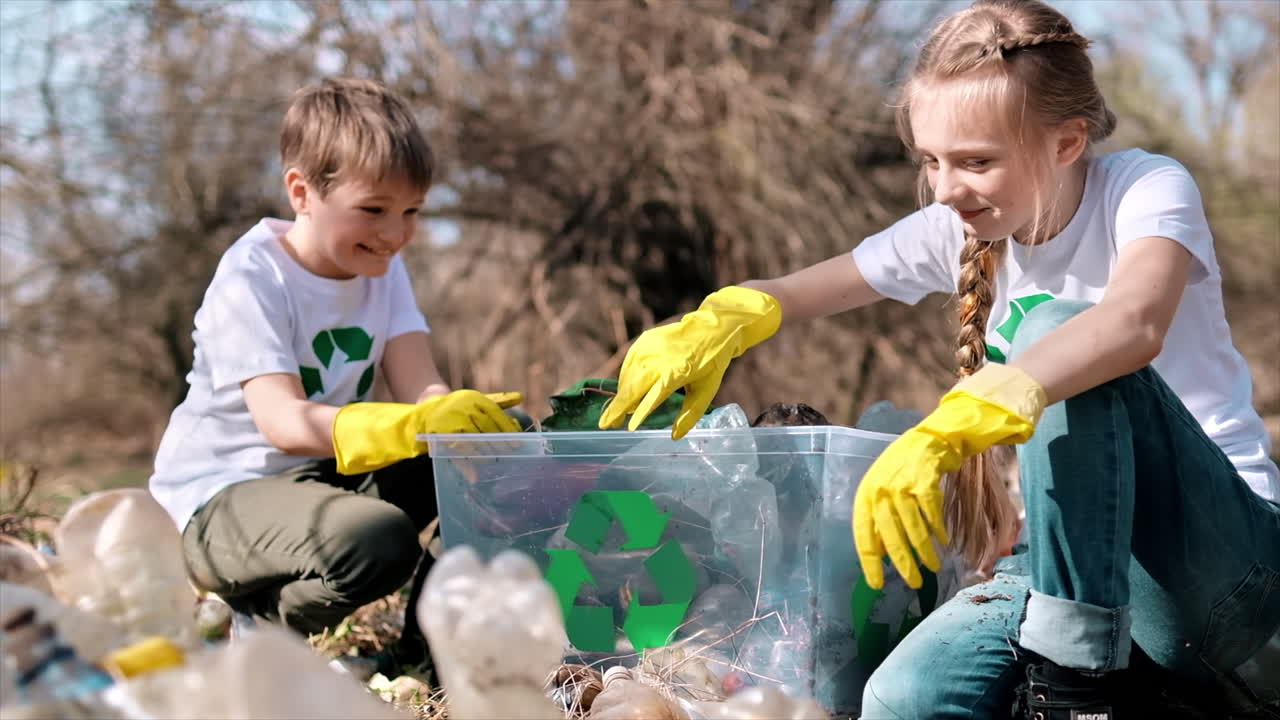 Boy and girl collecting plastic garbage in a container in a polluted clearing, recycling signs on the T-shirts. Slow motion