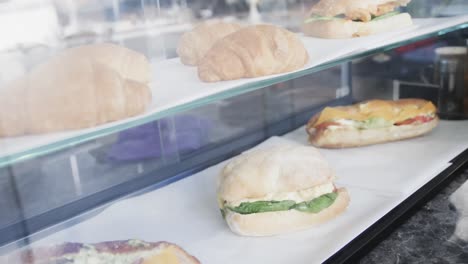 close up of fresh and tasty croissants and sandwiches over glass in bakery in slow motion