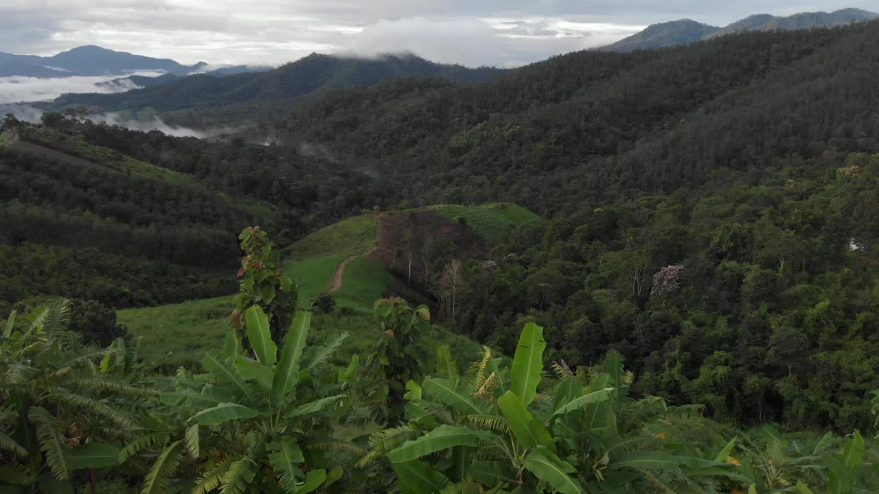 Drone reveal fly over the remote countryside hills of Pai, Thailand covered in rolling hills of green fields and thick cloud during monsoon season