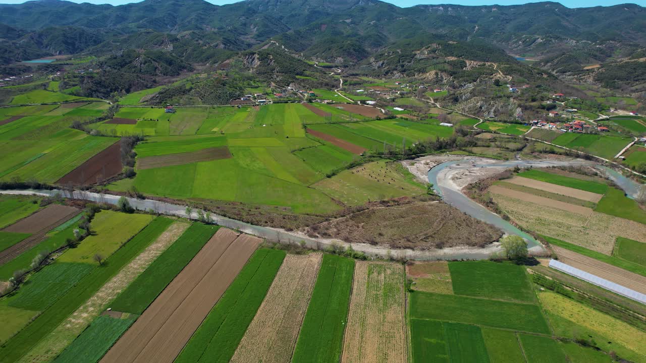 el río fluye a través de parcelas verdes en un paisaje de pueblo: tierra cultivada que prospera en primavera, enclavada en un hermoso valle en albania
