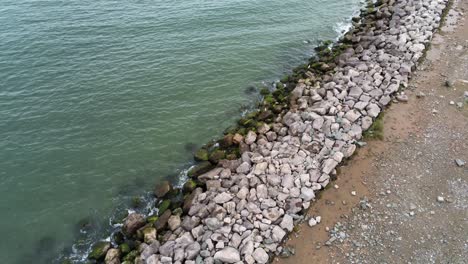 Aerial-view-above-splashing-ocean-tide-breaking-on-rocky-coastal-shoreline-rising-tilt-down