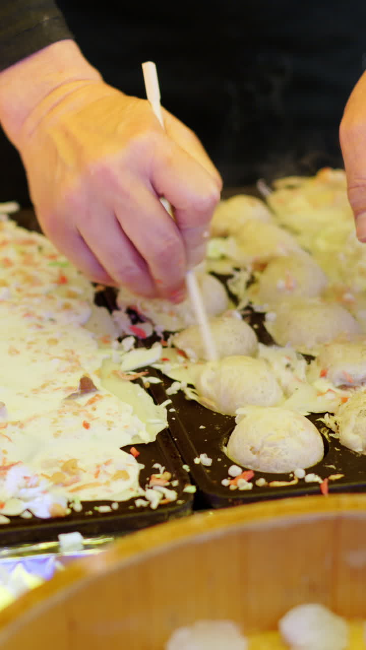 Close up of squid dumplings being cooked on a cast iron takoyaki grill pan at a street food market in Japan. Vertical