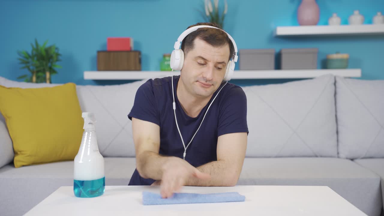 hombre involuntariamente, infeliz, escuchando música con auriculares mientras limpia.