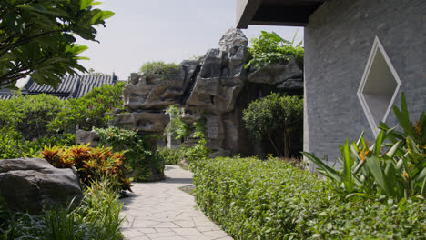 typical chinese garden with green vegetation next to typical chinese construction