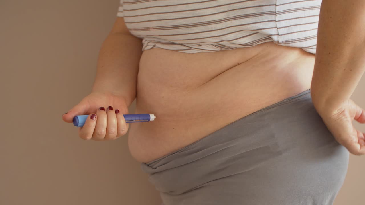 Donna in sovrappeso che si inietta un farmaco per il diabete nello stomaco.