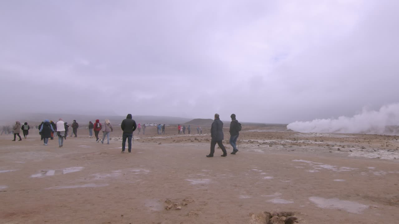 Tourists explore the steaming geothermal fields of Námaskarð under an overcast sky in Iceland