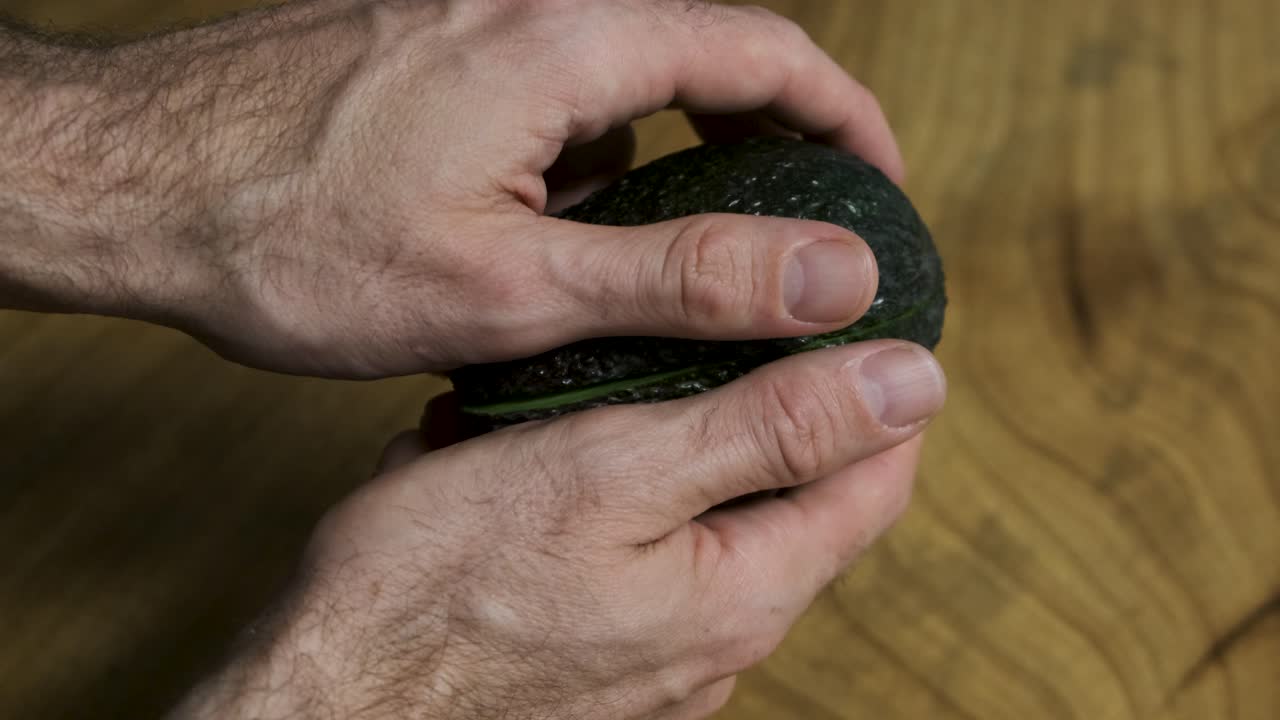 나무 테이블 배경 에 아보카도 를 절반 으로 열고 있는 젊은 남자