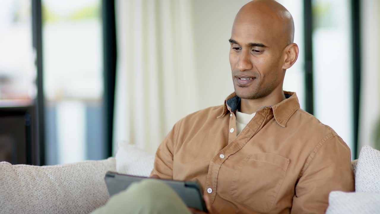 Uomo sui 30 anni che riceve contenuti e sorride con un tablet sul divano, navigando nell'interfaccia.