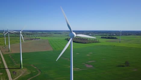 aerial view of wind turbines generating renewable energy in the wind farm, sunny spring day, low flyover over green agricultural cereal fields, countryside roads, drone dolly shot moving left