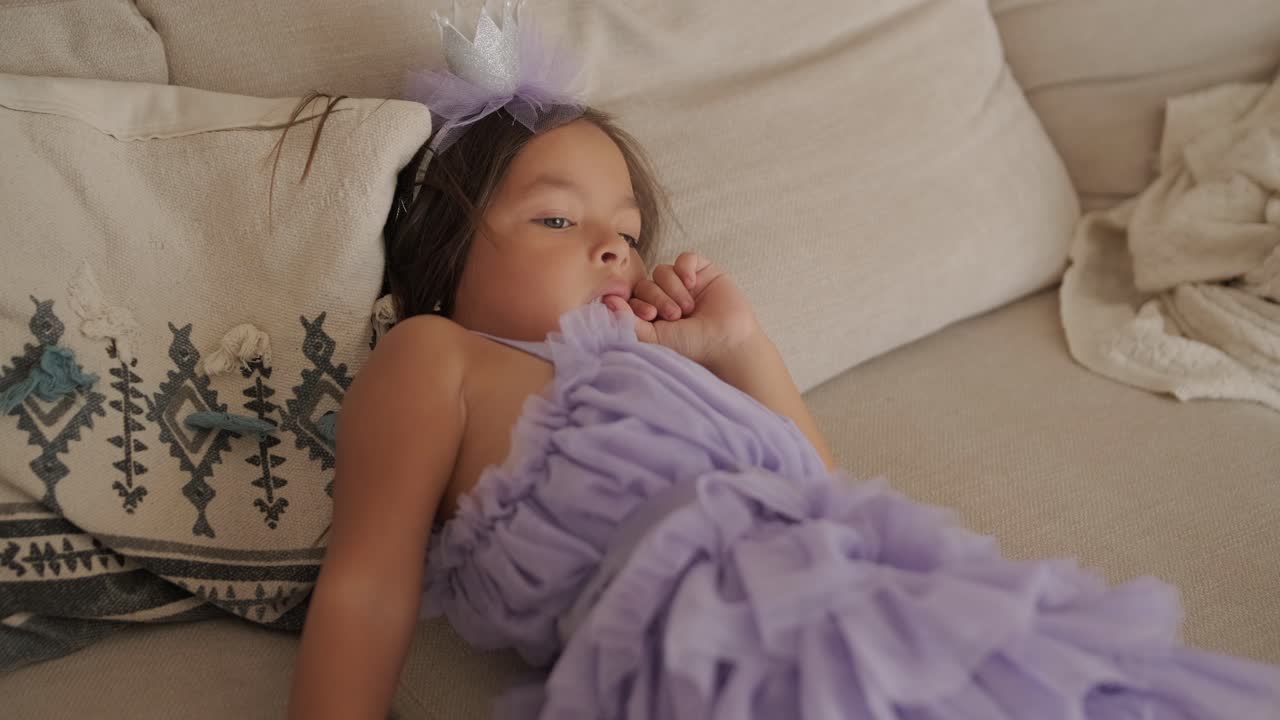 드레스를 입은 작은 소녀가 거실의 소파에서 tv를 보고 있습니다.