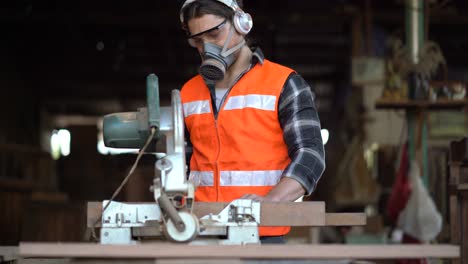 carpintero usando sierra circular cortando tabla de madera en el taller. joven constructor tabla de aserrar. artesano usando máscara de protección, protectores auditivos y gafas de seguridad.