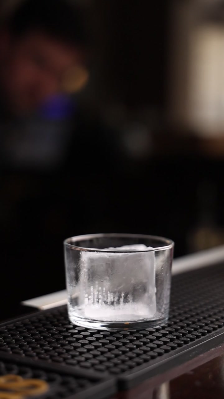 Un grande cubetto di ghiaccio in un bicchiere su un tappetino da bar