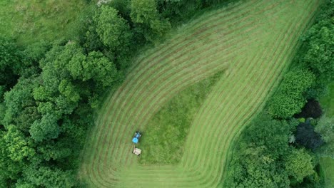 Vogelperspektive-Eines-Blauen-Traktors,-Der-Ein-Kleines,-Seltsam-Geformtes-Grasfeld-Schneidet