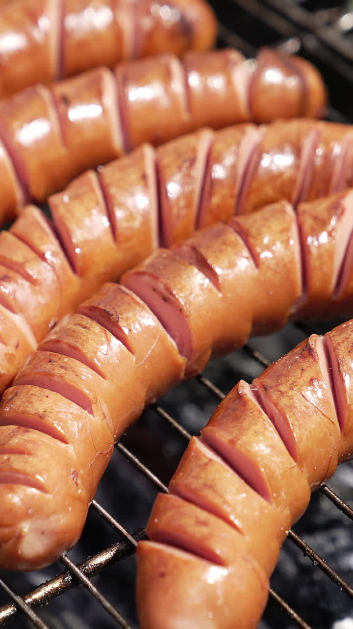 Sausages on a barbeque grill. Juicy sausages cooking over hot charcoal in smoke. Delicious food on a grill grate. Hand of chef turning sausages during cooking. Vertical video