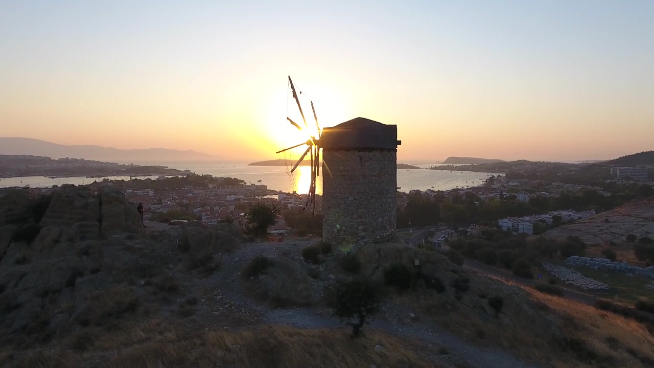 Antigo Moinho de Vento de Pedra com Vista para uma Cidade Costeira ao Pôr do Sol