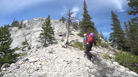 woman with backpack on difficult hiking trail, climbing under rocky summit