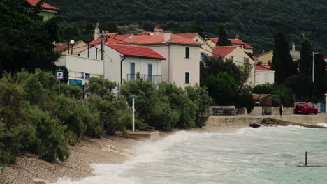 wide view of martinscica coastline and homes with orange roofs on stormy day, ocean waves crash violently