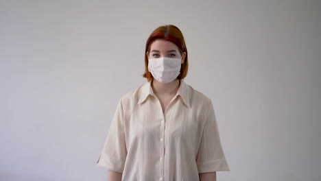Woman-showing-thumb-up-and-pointing-her-medical-face-mask-with-gloves.-Copy-space-and-white-background.