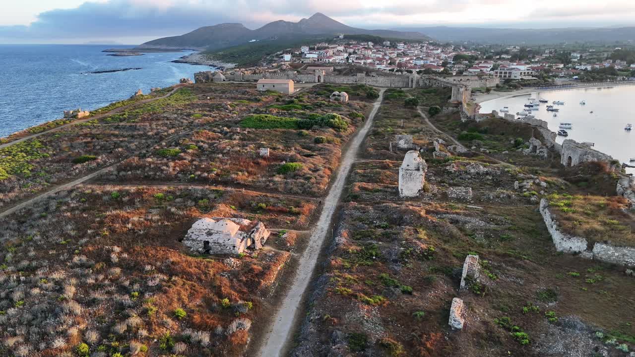 Methoni,Messenia,Peloponnese,Aerial view forward and over Methoni Castle ruins towards town with white houses during golden hour with white clouds and hills at the back ground