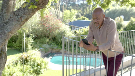 happy senior biracial man using smartphone at balcony at home, slow motion